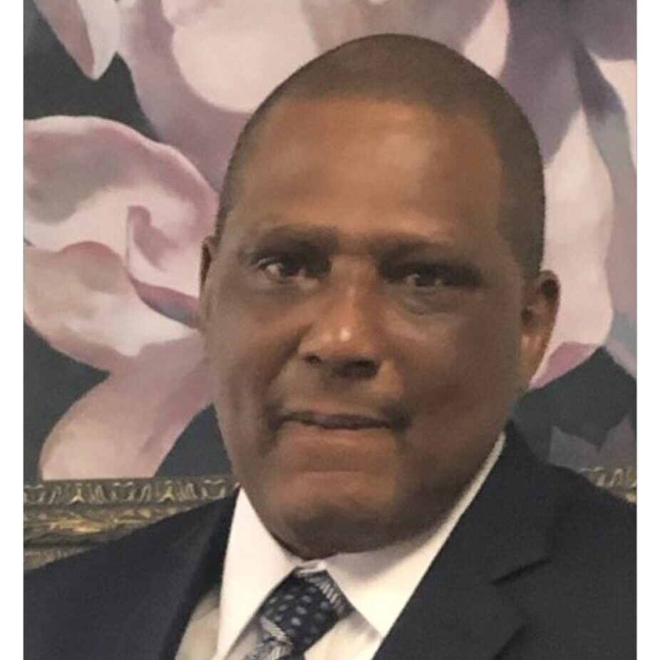 A man in suit and tie standing next to flowers.
