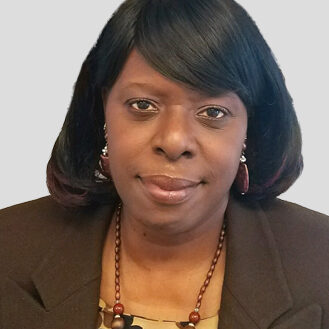 A woman in brown jacket and necklace posing for the camera.